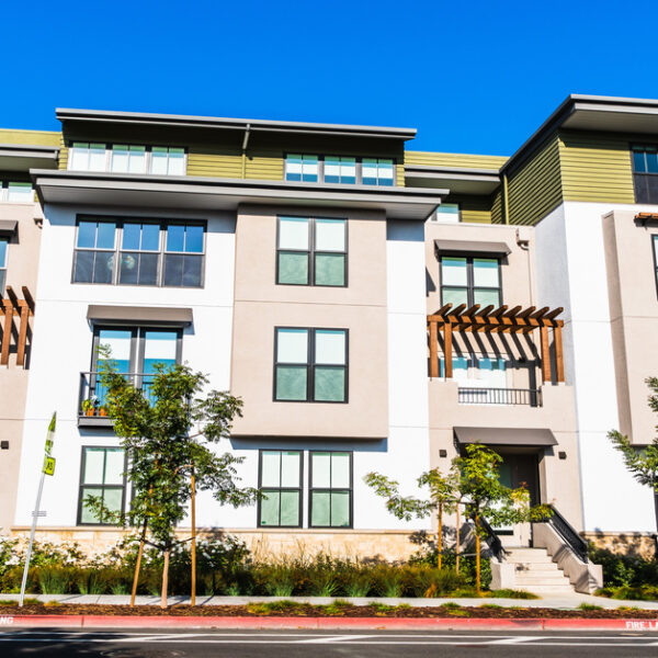 A street view of an apartment complex with pergolas on the balconies and trees and grasses lining the sidewalk.