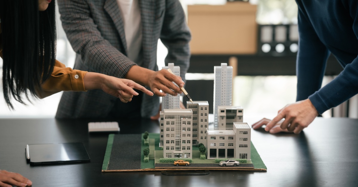 A group of people gathered around a small-scale model of a residential building and cityscape.