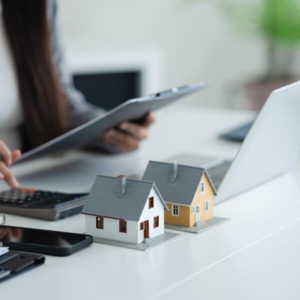 A person reviewing home loan documents beside a calculator, pen, keys, and house model on an office desk.