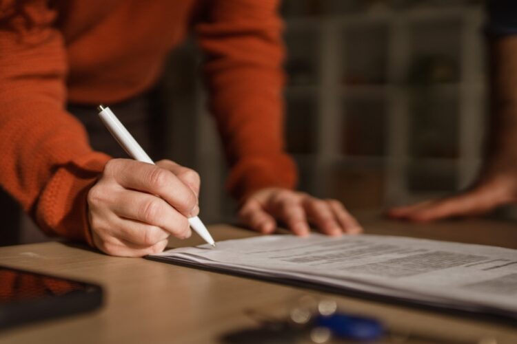 A person signing a real estate contract with a pen on a desk beside keys and paperwork in a close-up view.