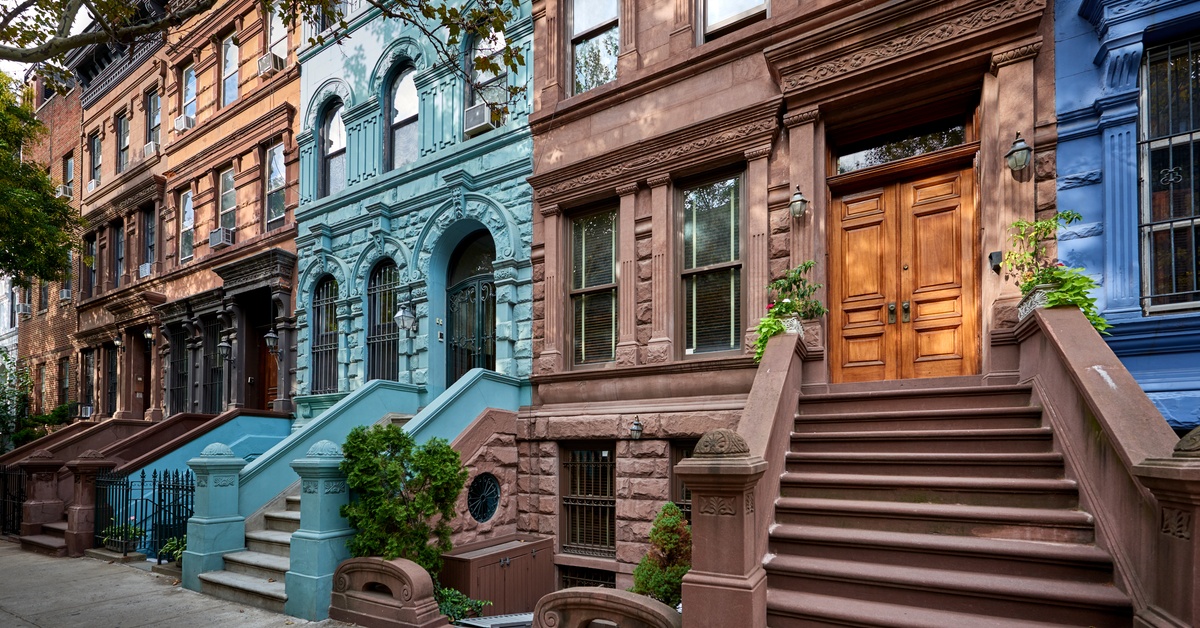 A row of historic brownstone home facades in various paint colors on a street in Manhattan, New York City.