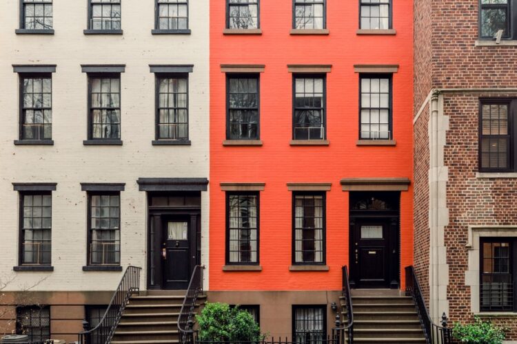 The facades of several neighborhood homes next to each other in different colors on a New York Street.
