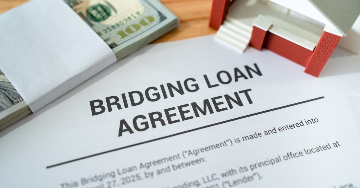 A close-up of a document with the heading "Bridging Loan Agreement" next to a stack of money and a model home.