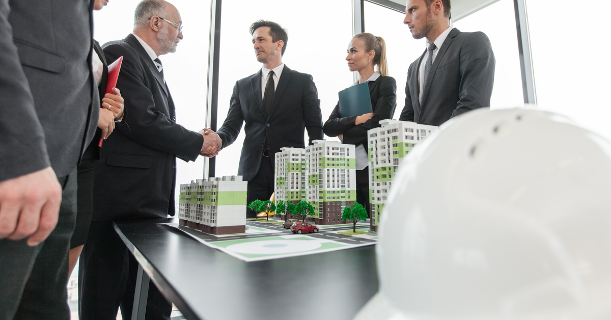 A group of people gathered around a model of an apartment complex on a table, with two people shaking hands.