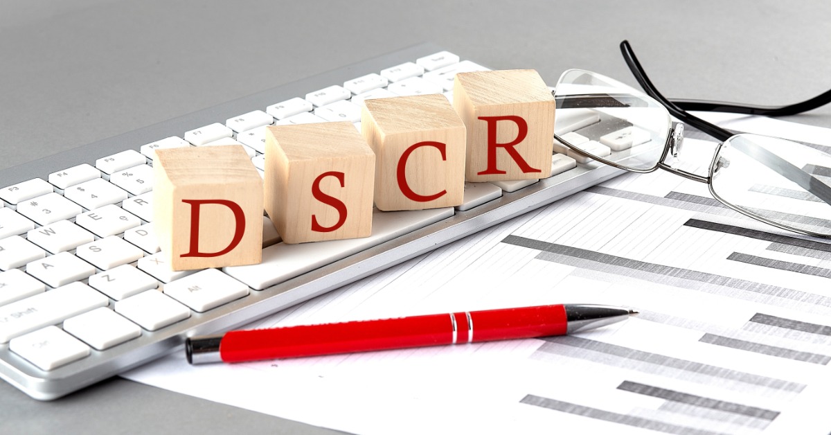 wooden letter cubes spelling DSCR placed on a computer keyboard with a printed chart and pen in the background.
