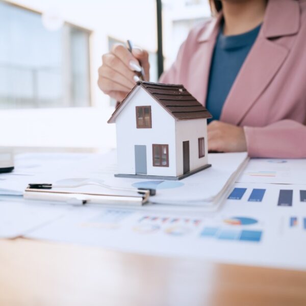a woman reviewing financial charts at a desk beside a small house model, calculator, and printed documents.