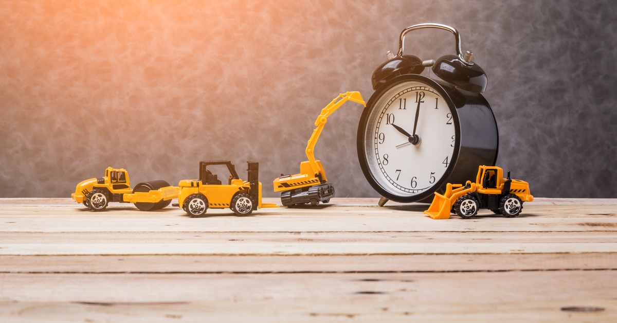 A black traditional clock sits on a wooden bench with small, orange construction toys scattered around it.