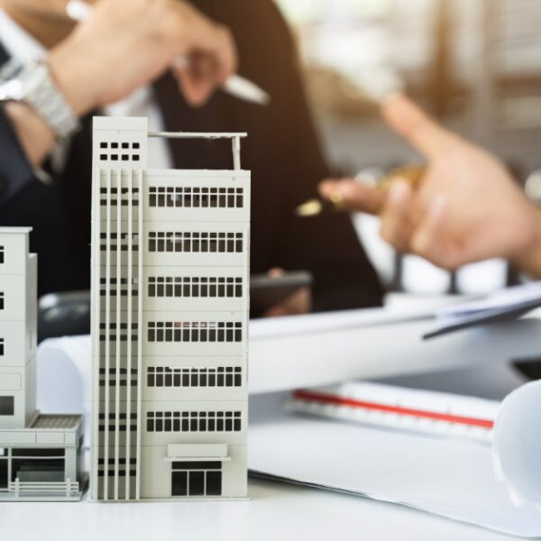 Miniature condominium models on a desk near a person holding a pen above a contract form on a clipboard.