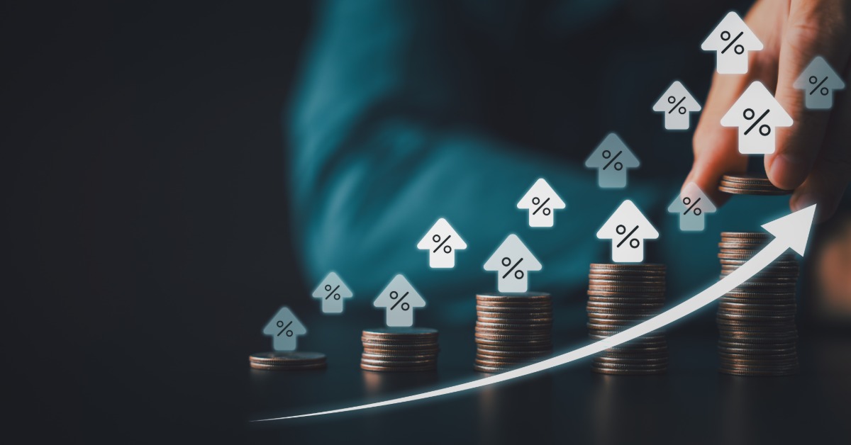 Stacks of coins beside percentage symbols, small house icons, and an upward arrow on a blue financial graphic.