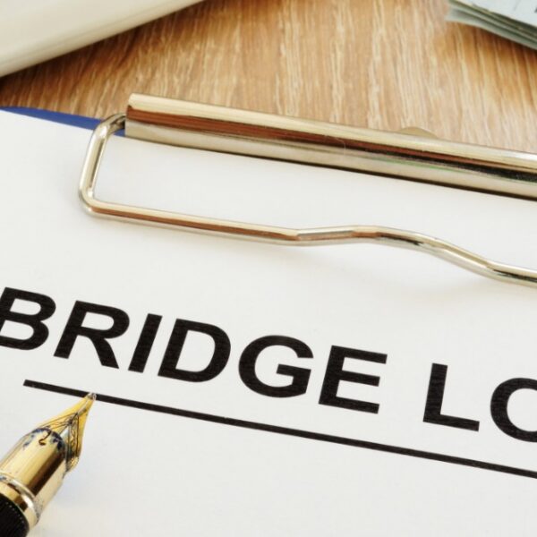 A bridge loan document on a clipboard beside a calculator, fountain pen, and a stack of hundred-dollar bills.