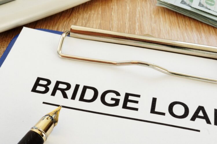 A bridge loan document on a clipboard beside a calculator, fountain pen, and a stack of hundred-dollar bills.